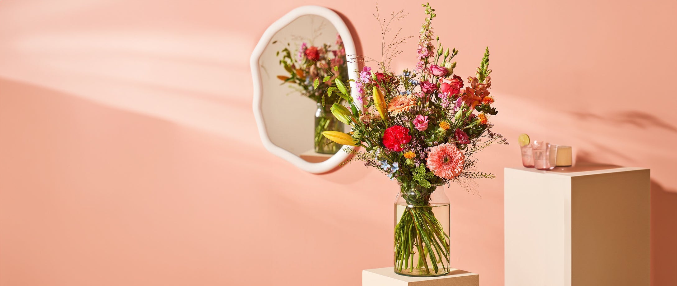 Boeket kleurrijke bloemen in een glazen vaas, klaar om bezorgd te worden, tegen een roze achtergrond.