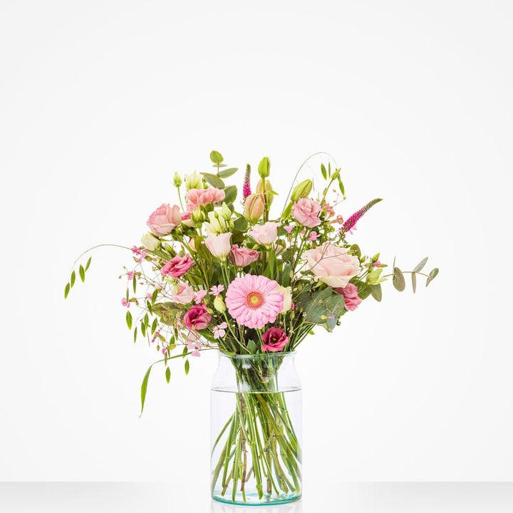 Klein boeket in een glazen vaas met roze gerbera's, rozen en andere bloemen.