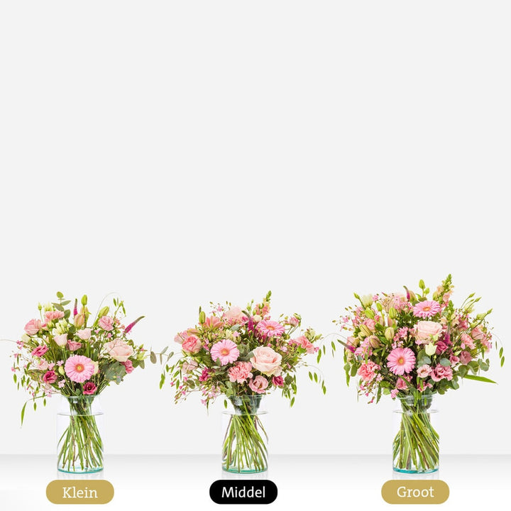 Drie boeketten in glazen vazen met roze gerbera's, rozen en andere bloemen, in klein, middel en groot formaat naast elkaar.