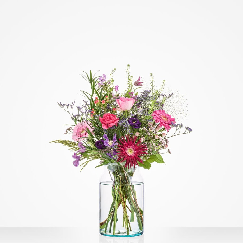 Klein verjaardagboeket in een glazen vaas met roze, paarse en rode bloemen tegen een witte achtergrond.