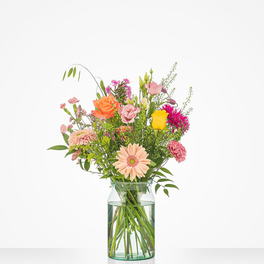 Klein boeket met diverse bloemen in pastel- en felle tinten, waaronder gerbera’s en rozen, gepresenteerd in een glazen vaas.