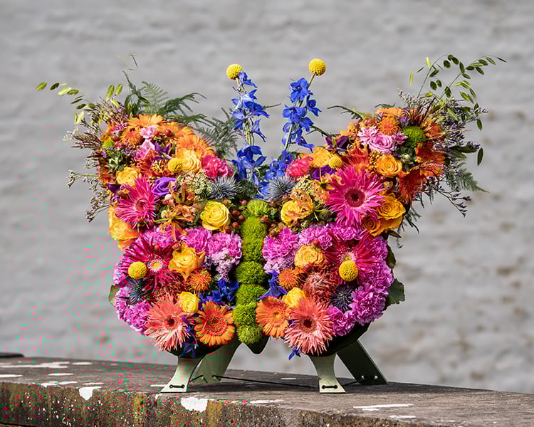 Vlindervormig rouwwerk met kleurrijke bloemen, ontworpen door Buurtbloemist voor een uniek afscheid.
