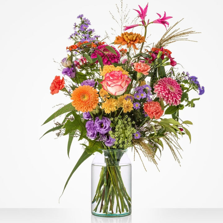 Groot boeket met roze rozen, paarse bloemen en diverse seizoensbloemen in glazen vaas.