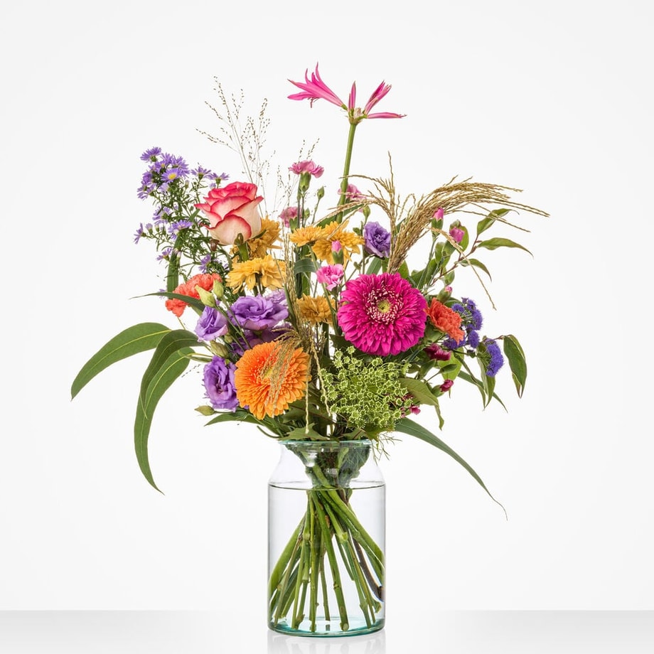 Klein boeket met roze gerbera’s, paarse lisianthus en kleurrijke bloemen in glazen vaas.