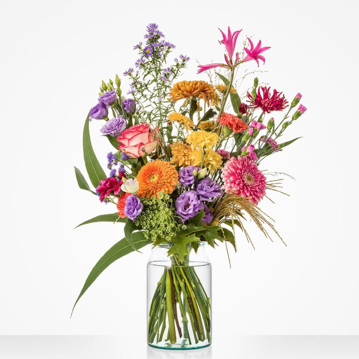 Middelgroot boeket met roze rozen, oranje bloemen en groene bladeren in glazen vaas.