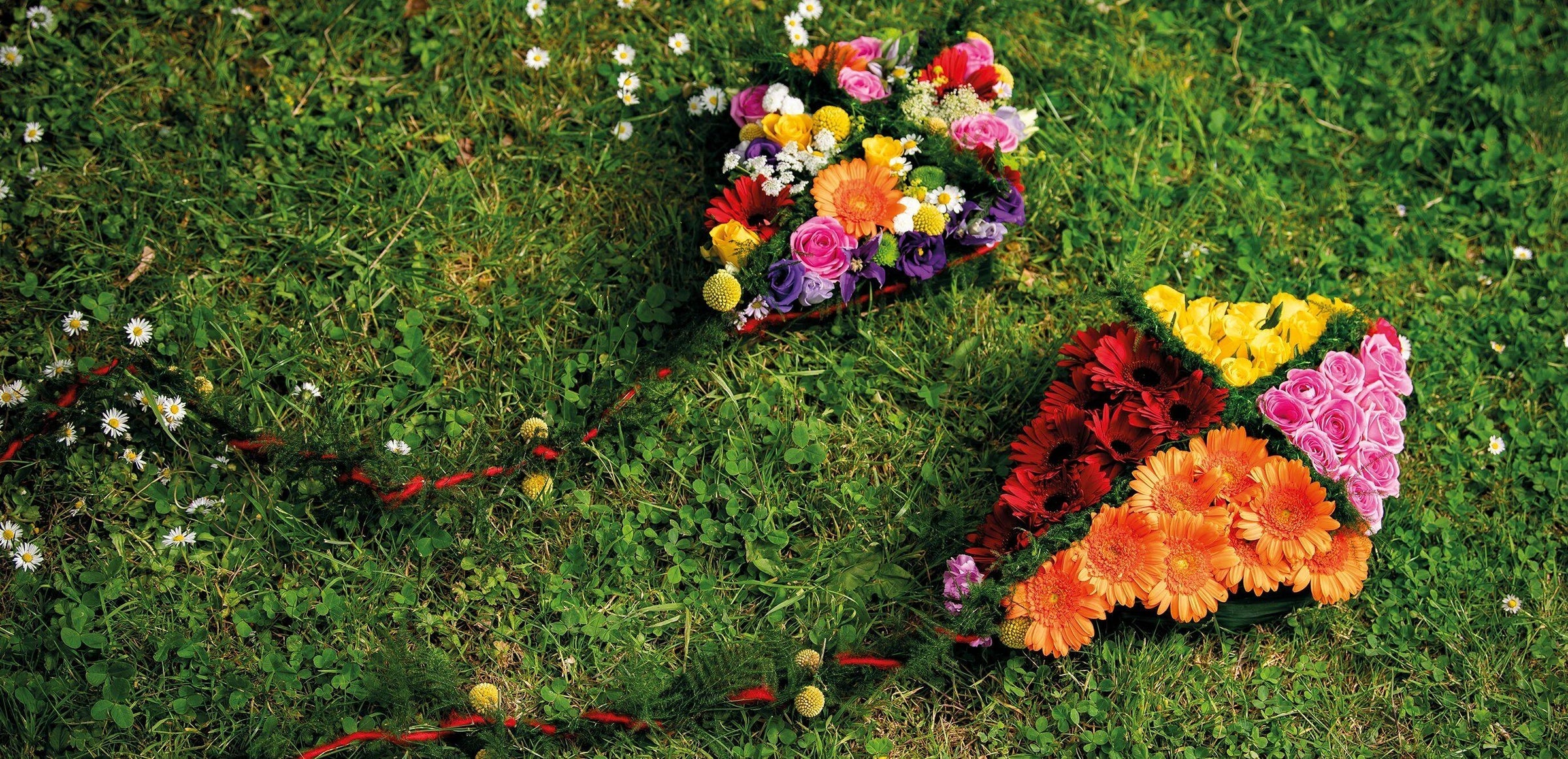 Rouwbloemstukken in vlieger-vorm, versierd met kleurrijke bloemen, liggend op gras.