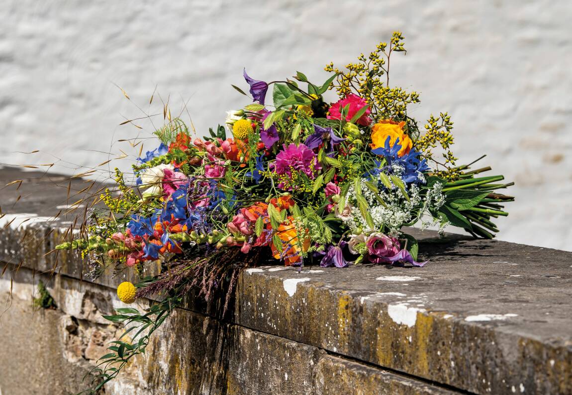 Rouwboeket met kleurrijke bloemen, liggend op een stenen rand tegen een lichte achtergrond.