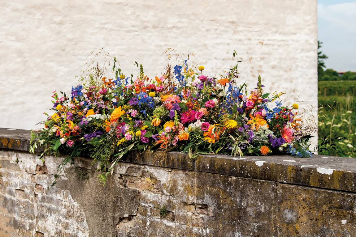 Kistbedekking met kleurrijke bloemen, liggend op een stenen rand tegen een lichte achtergrond.