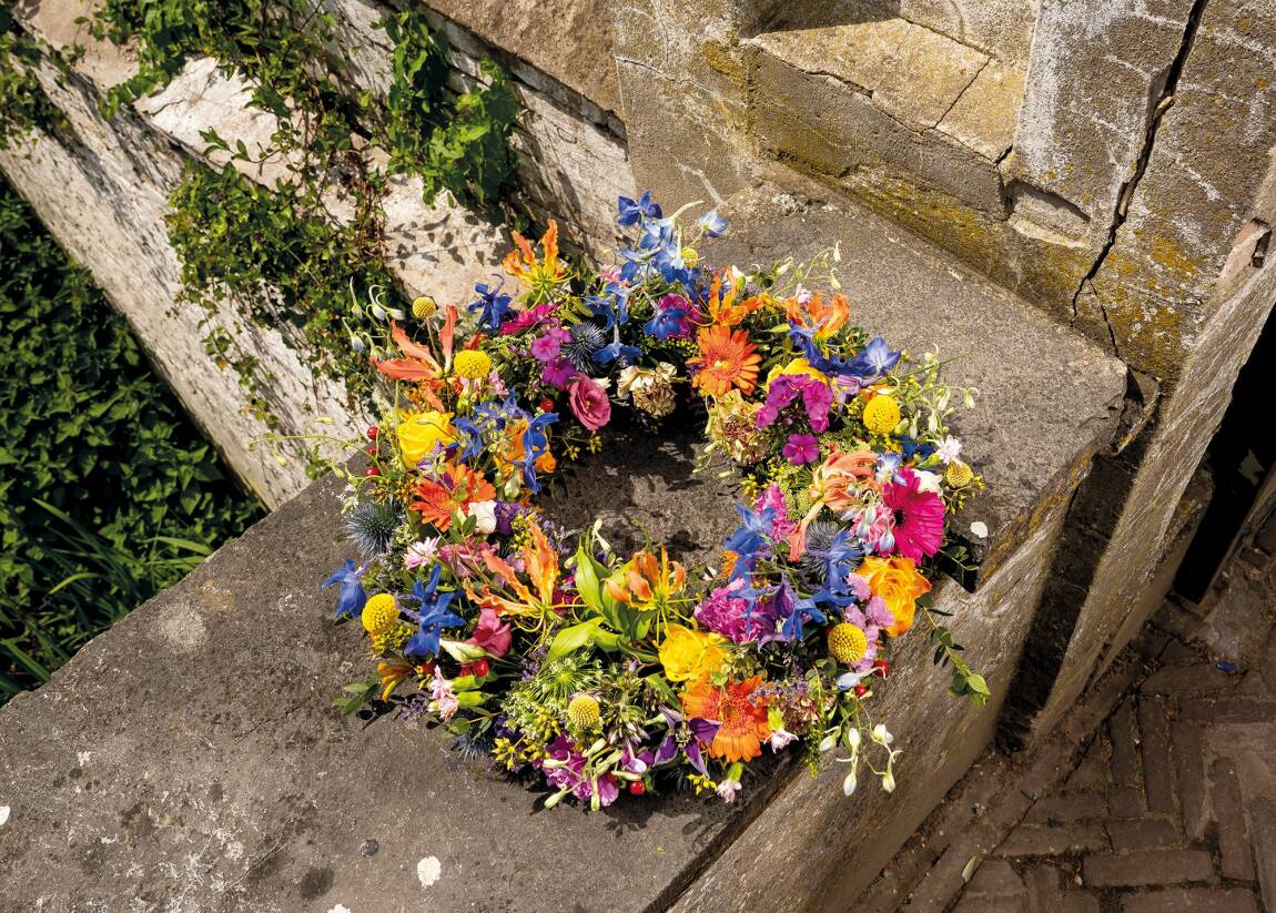 Kleurrijke rouwkrans met lint en bloemen, rustend op een stenen rand, geschikt voor begrafenissen of herdenkingen.