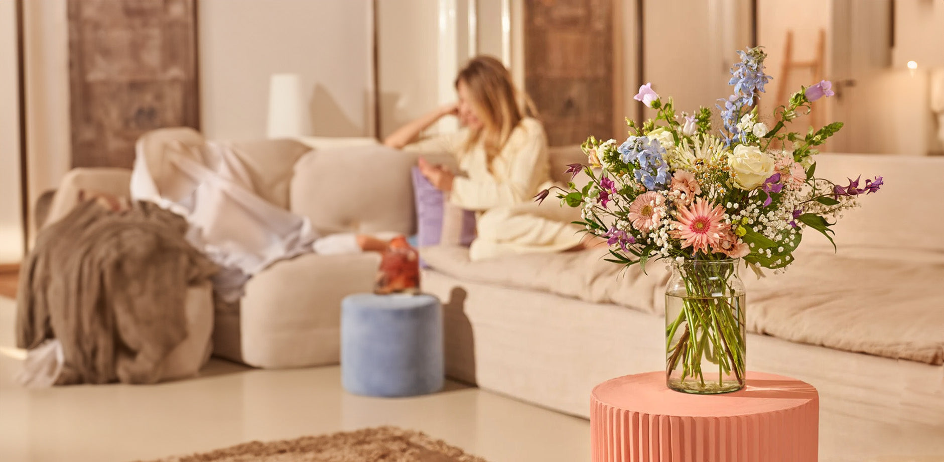 Geboorte boeket met zachte kleuren bloemen in een glazen vaas, geschikt om een geboorte te vieren, geplaatst op een roze tafel in een huiselijke setting.