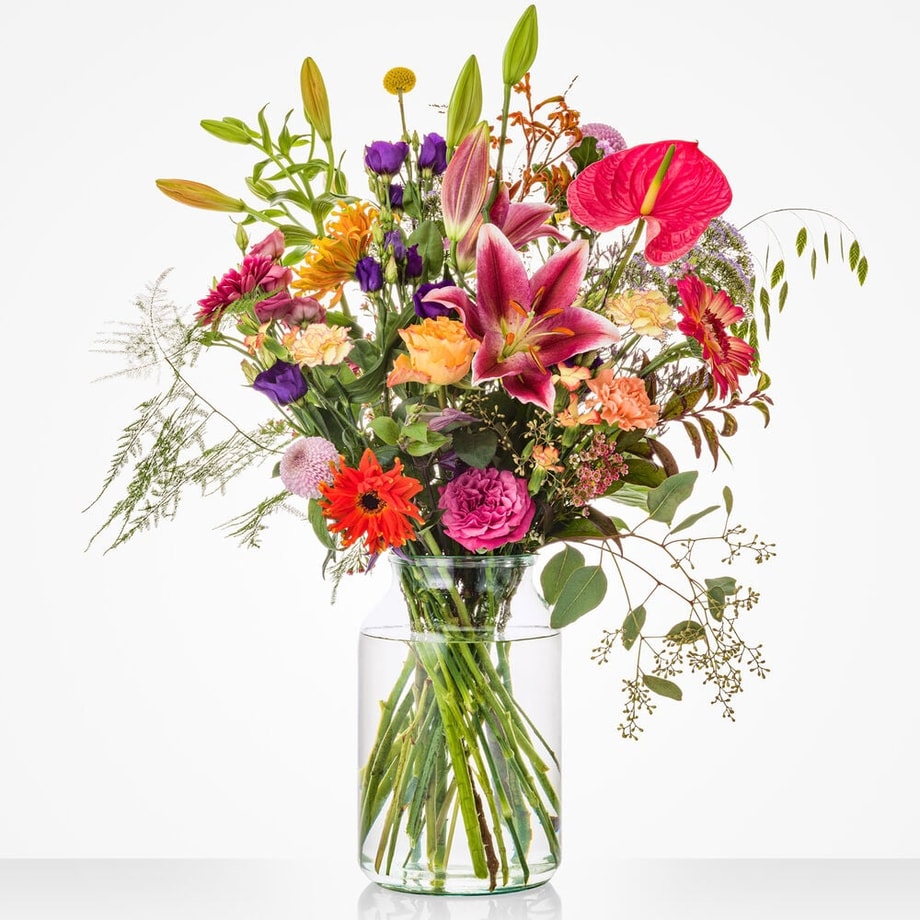 Kleurrijk groot boeket in een glazen vaas met anthurium, lelie, roos en andere bloemen.