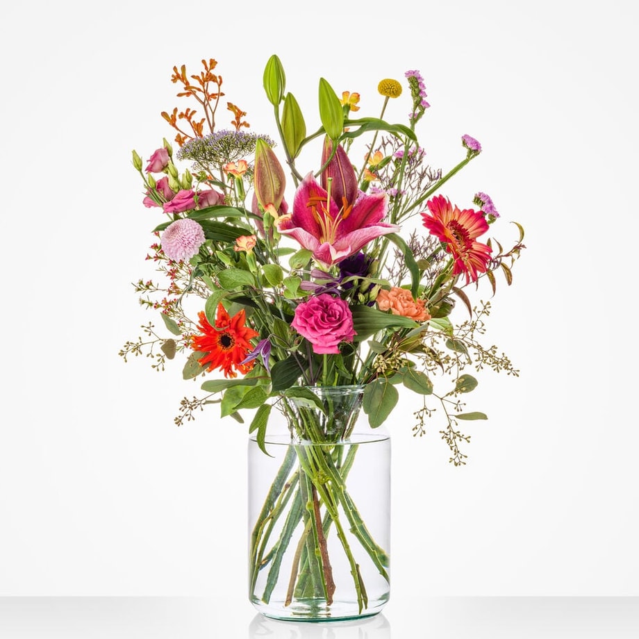 Kleurrijk klein boeket in een glazen vaas met anthurium, lelie, roos en andere bloemen.