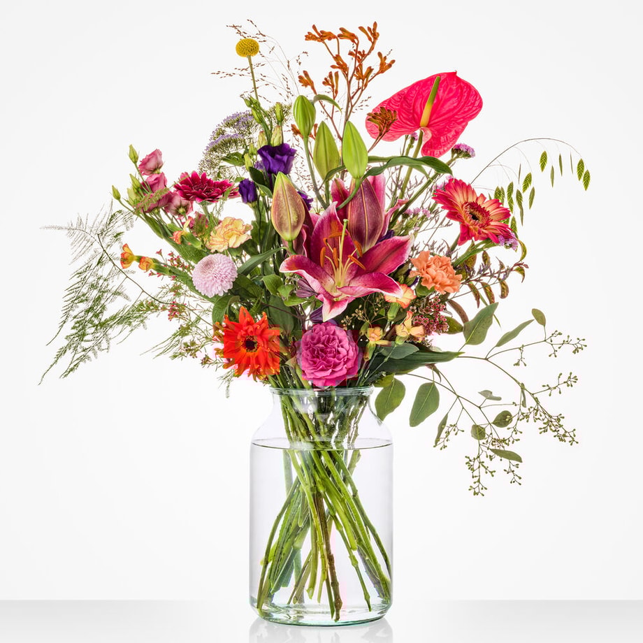 Kleurrijk middelgroot boeket in een glazen vaas met anthurium, lelie, roos en andere bloemen.