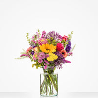 Kleurrijk groot boeket in een glazen vaas met zonnebloemen, rozen en andere bloemen.
