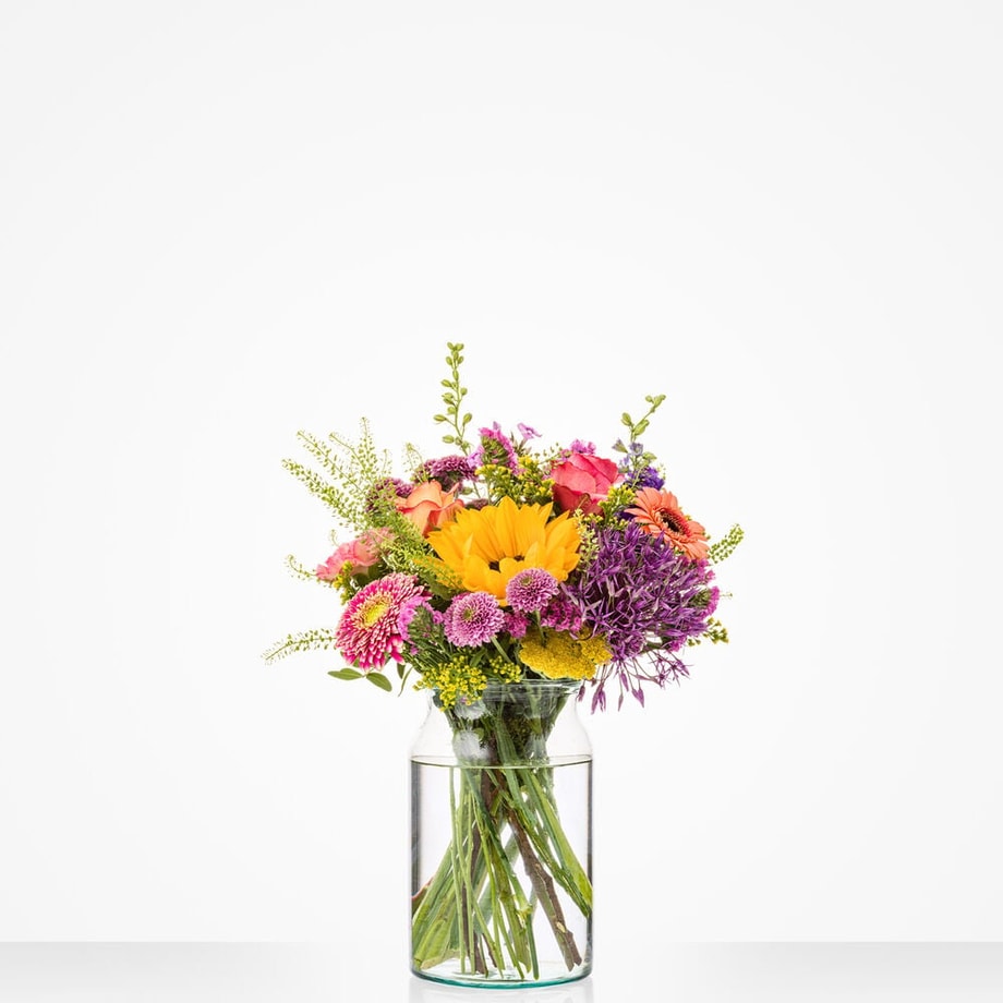 Kleurrijk klein boeket in een glazen vaas met zonnebloemen, rozen en andere bloemen.