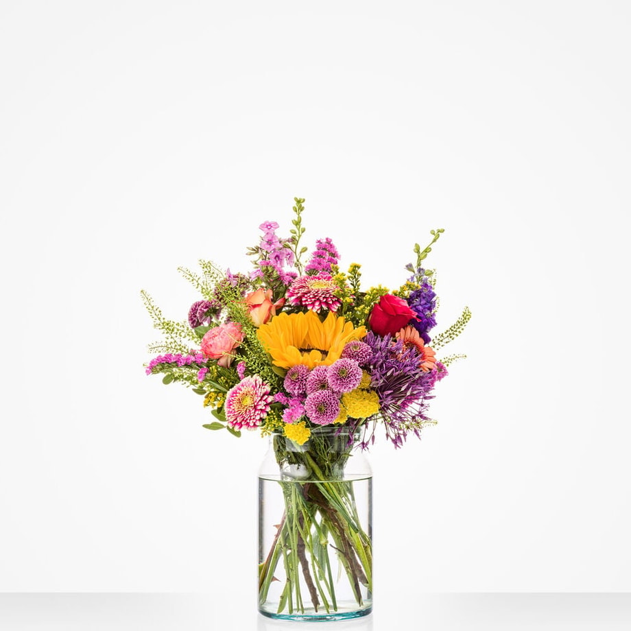 Kleurrijk middelgroot boeket in een glazen vaas met zonnebloemen, rozen en andere bloemen.
