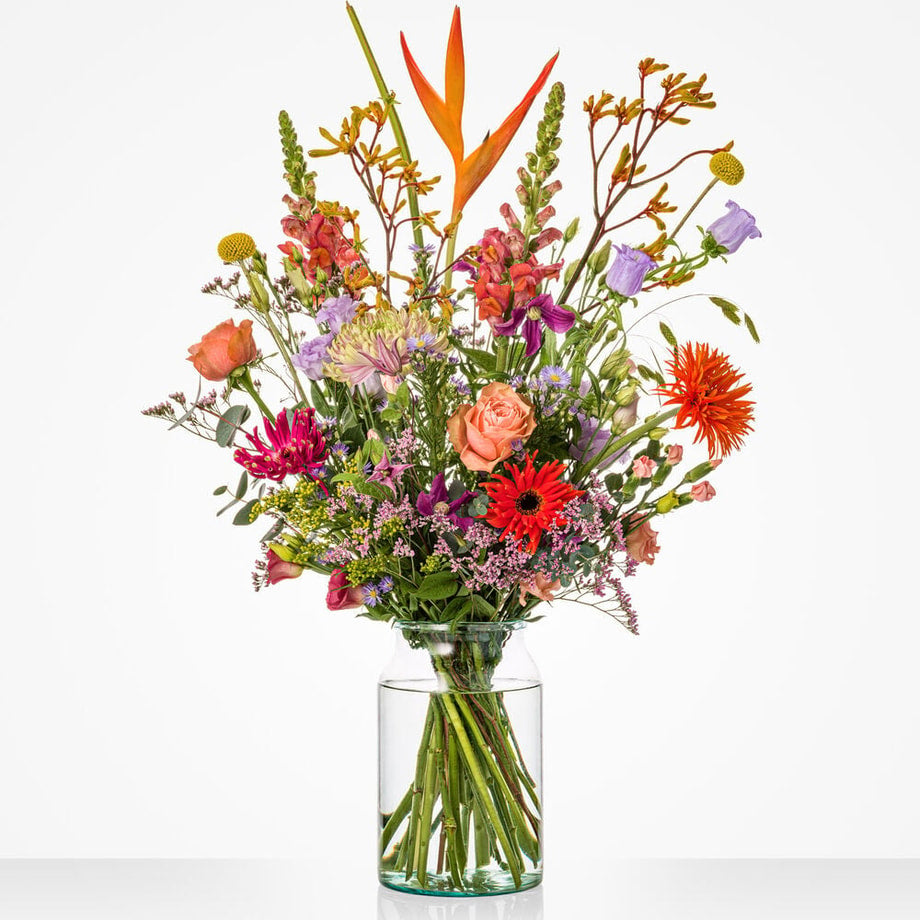 Kleurrijk groot boeket in een glazen vaas met paradijsvogelbloemen, rozen en gerbera's.