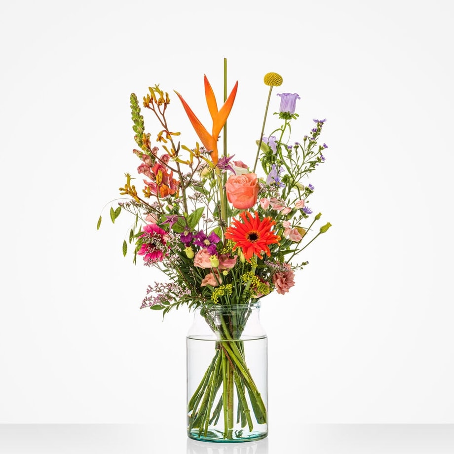 Kleurrijk klein boeket in een glazen vaas met paradijsvogelbloemen, rozen en gerbera's.