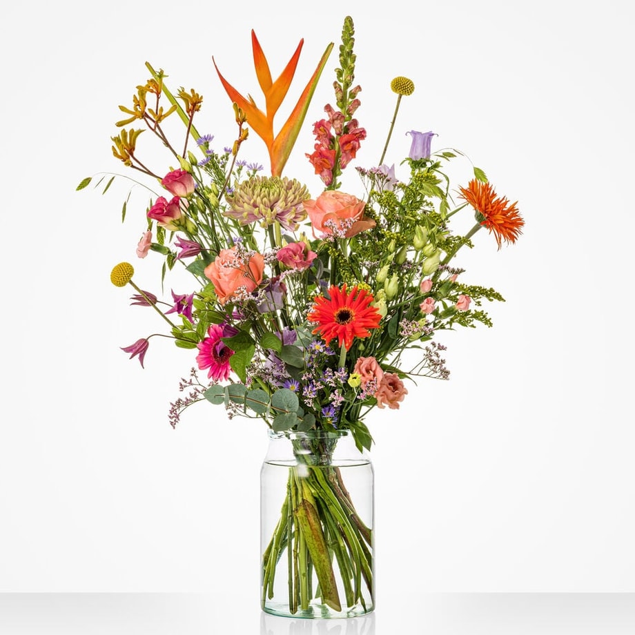Kleurrijk middelgroot boeket in een glazen vaas met paradijsvogelbloemen, rozen en gerbera's.
