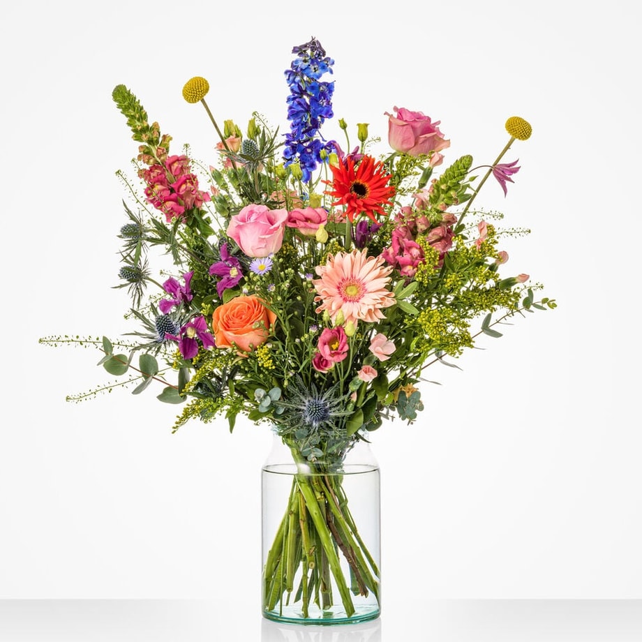 Kleurrijk groot boeket in een glazen vaas met delphinium, rozen, gerbera's en andere bloemen.