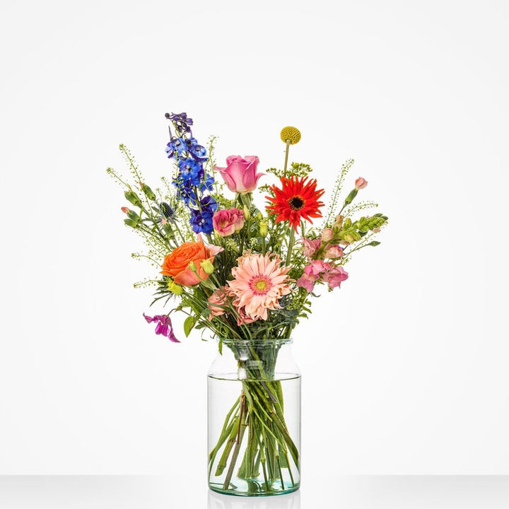 Kleurrijk klein boeket in een glazen vaas met delphinium, rozen, gerbera's en andere bloemen.