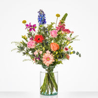 Kleurrijk middelgroot boeket in een glazen vaas met delphinium, rozen, gerbera's en andere bloemen.