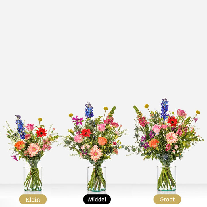 Drie kleurrijke boeketten in glazen vazen met delphinium, rozen, gerbera's en andere bloemen, in klein, middel en groot formaat naast elkaar.