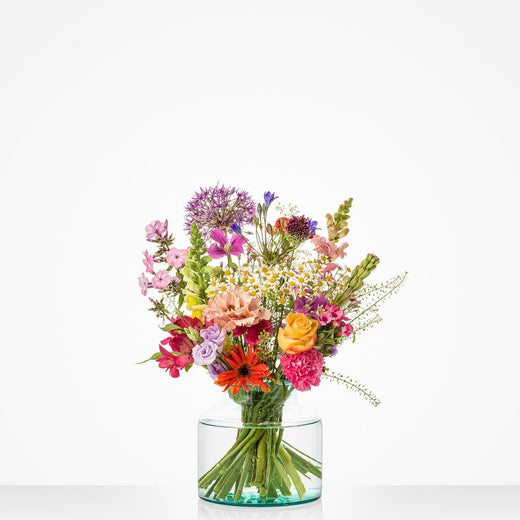 Middelgroot veldboeket met een mix van zomerse bloemen in verschillende kleuren zoals geel, roze, paars en oranje in een glazen vaas