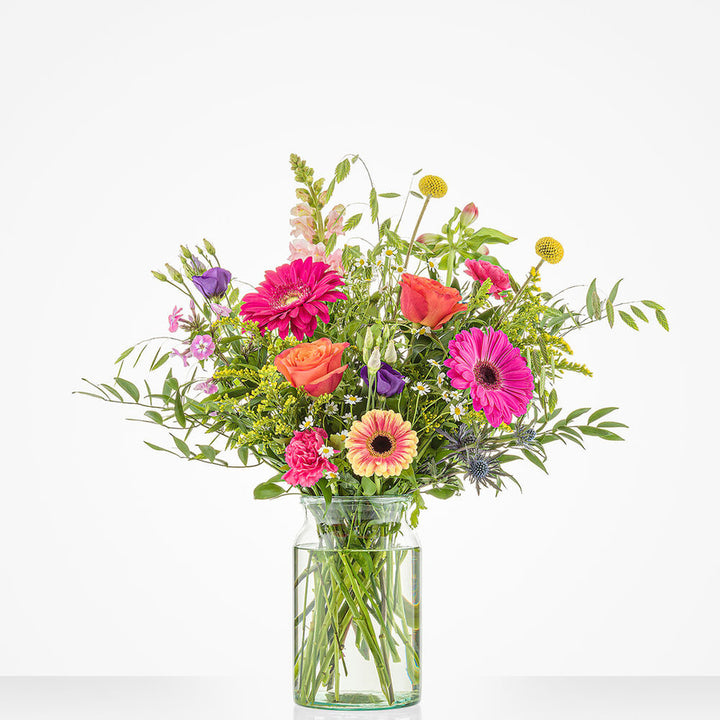 Bont gekleurd groot boeket in een glazen vaas met gerbera's, rozen en andere bloemen.