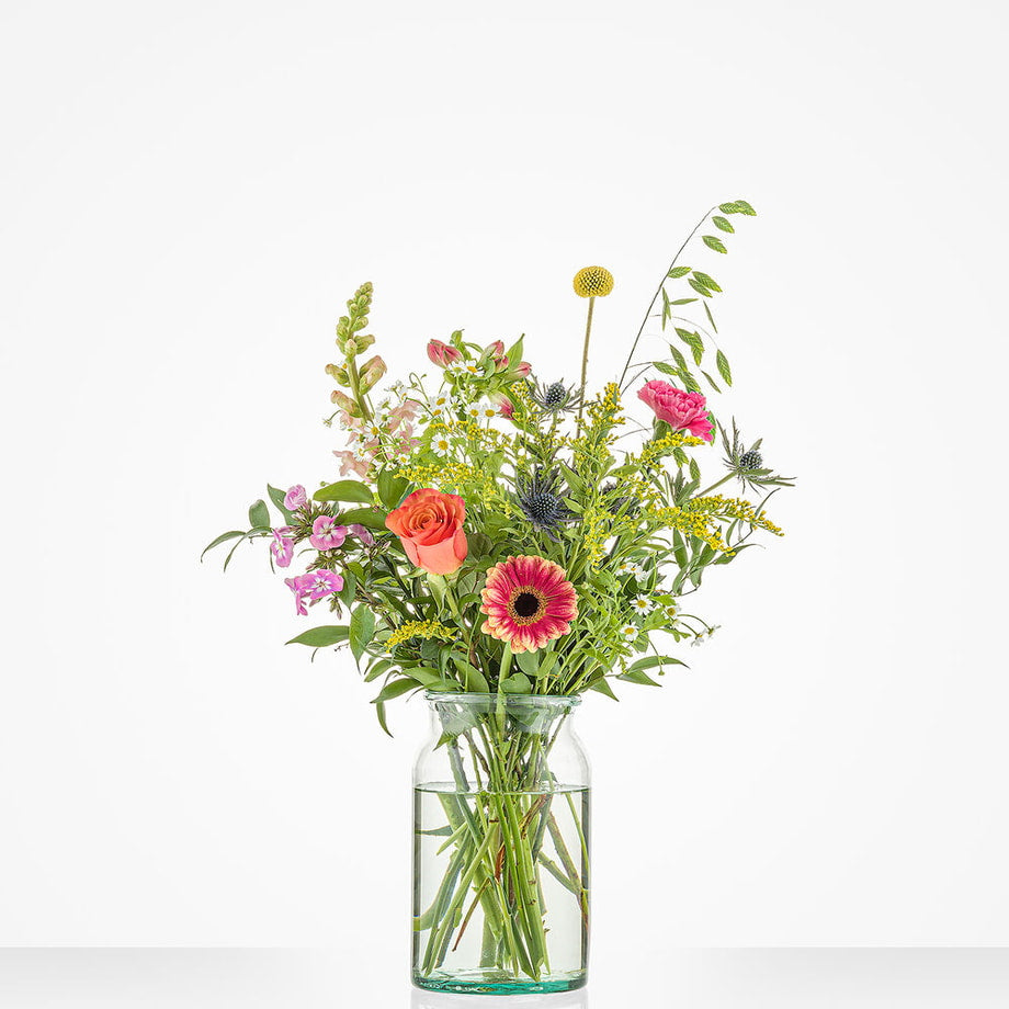 Bont gekleurd klein boeket in een glazen vaas met gerbera's, rozen en andere bloemen.