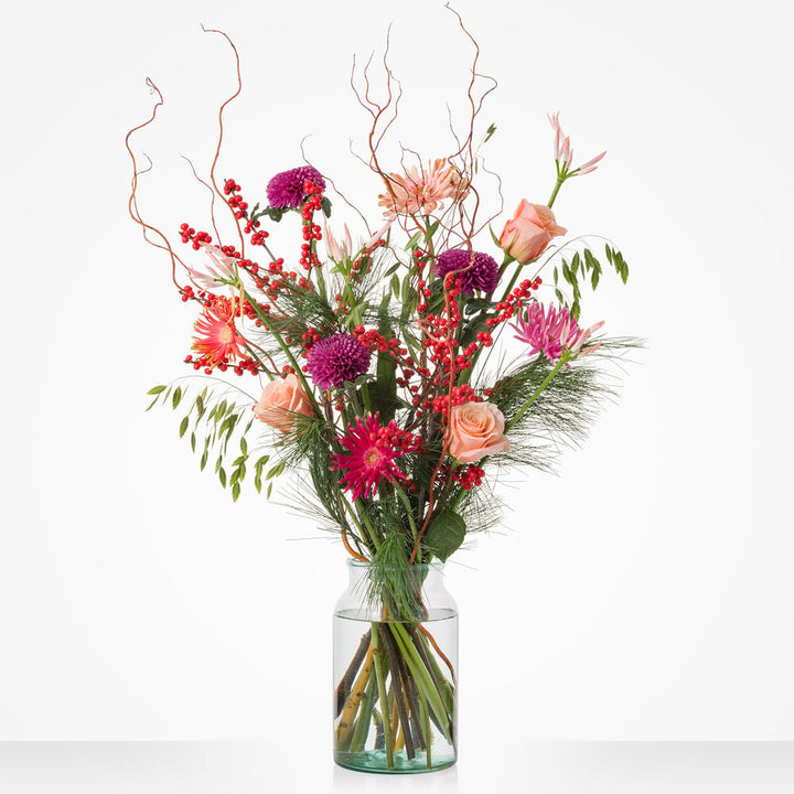 Christmas deluxe boeket met roze rozen, paarse bloemen en rode bessen in glazen vaas.