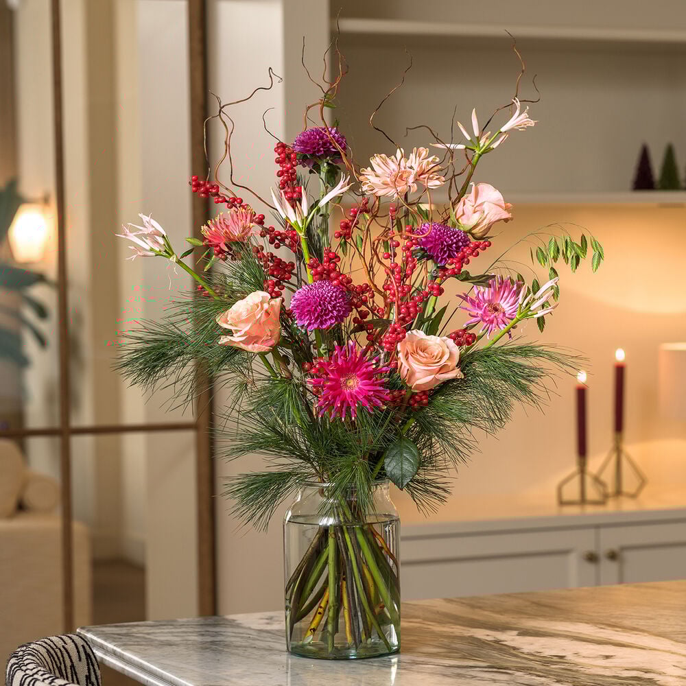 Christmas deluxe boeket met roze rozen, paarse bloemen en rode bessen in een sfeervol interieur.