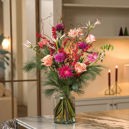 Christmas deluxe boeket met roze rozen, paarse bloemen en rode bessen in een sfeervol interieur.