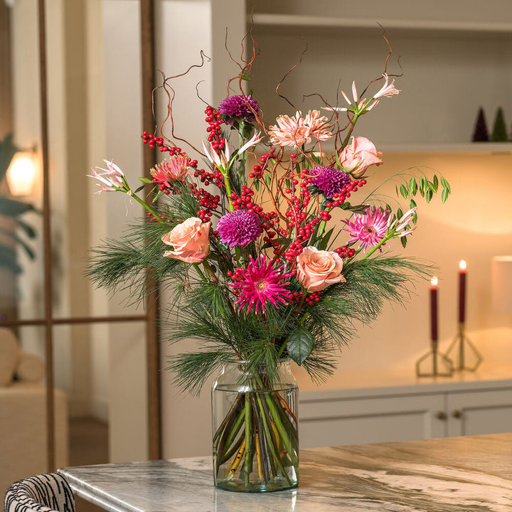 Christmas deluxe boeket met roze rozen, paarse bloemen en rode bessen in een sfeervol interieur.
