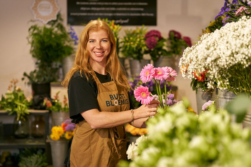 Bloemiste van Buurtbloemist met roze gerbera's in haar bloemenwinkel vol verse boeketten