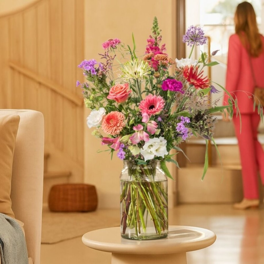 Sfeervolle woonkamer met het Denken aan boeket in een glazen vaas op een ronde tafel, vol roze, paarse en oranje bloemen.