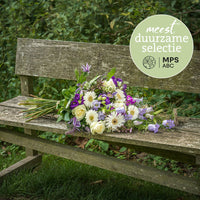 Duurzaam rouwboeket in zachte pasteltinten met witte en paarse bloemen, tegen een groene achtergrond.