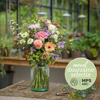Duurzaam pastelboeket met rozen, gerbera’s en veldbloemen in glazen vaas in kasomgeving