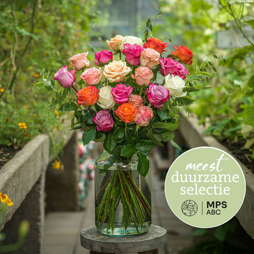 Duurzaam rozenboeket met roze, oranje en witte rozen in glazen vaas in een groene omgeving