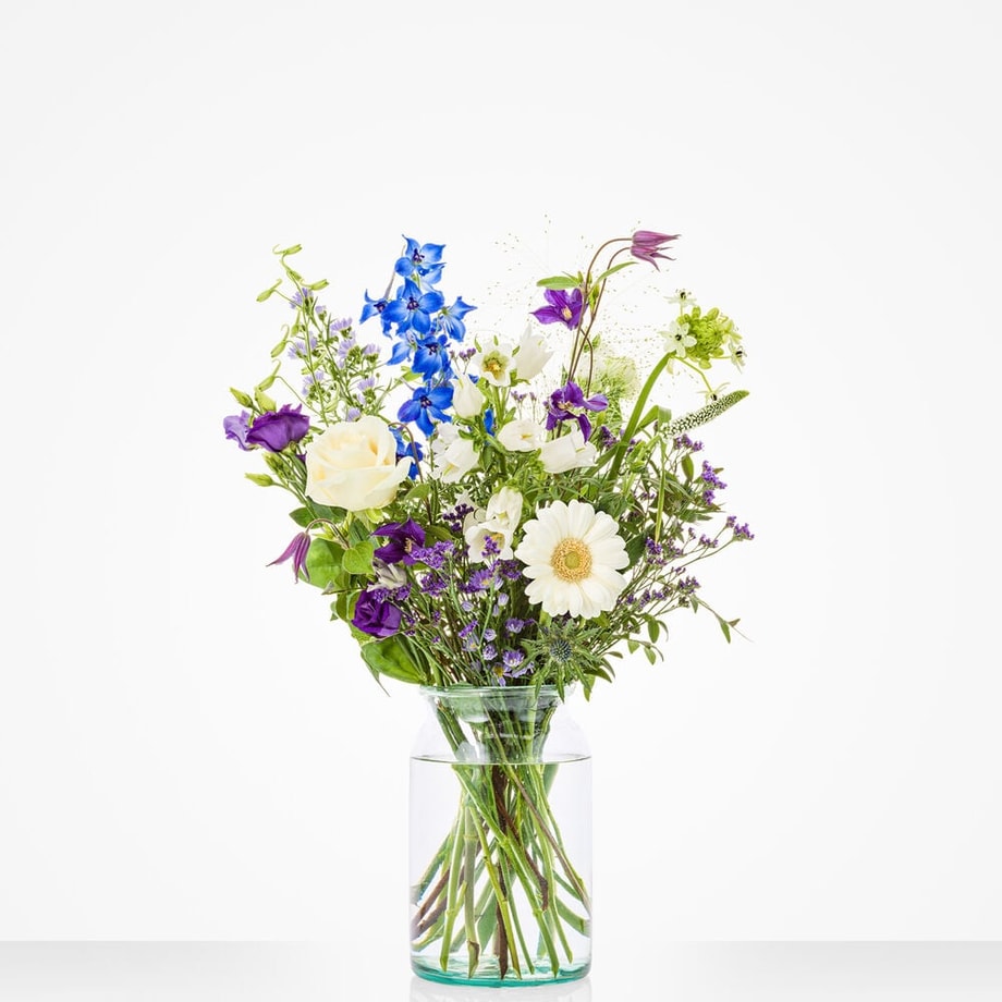 Klein boeket in een glazen vaas met witte rozen, blauwe bloemen en paarse accenten.