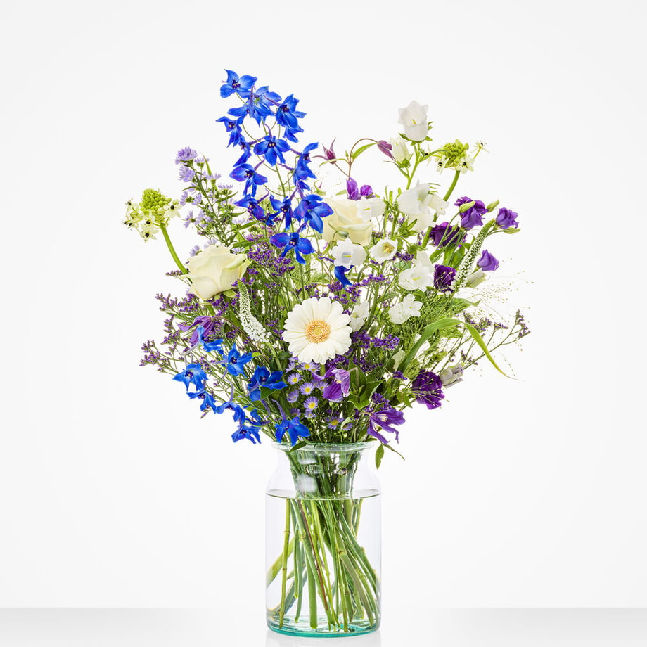 Middelgroot boeket in een glazen vaas met witte rozen, blauwe bloemen en paarse accenten.