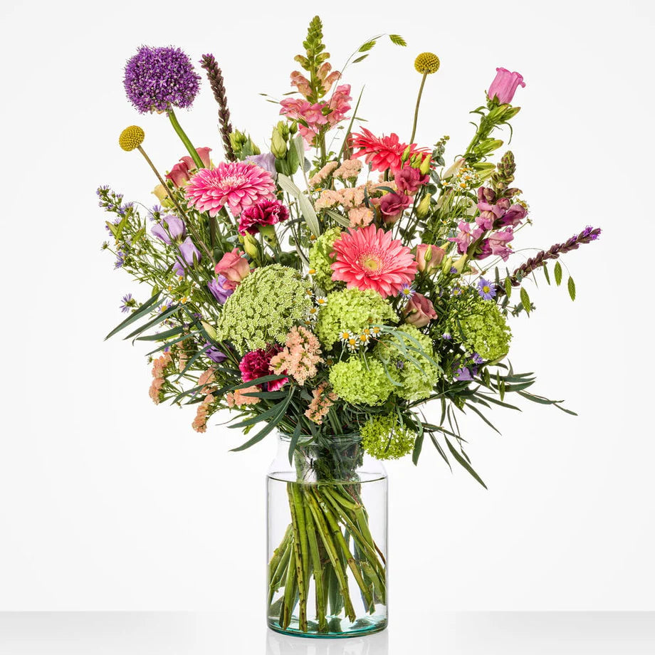 Gekleurd groot boeket in een glazen vaas met gerbera's, rozen en andere bloemen.