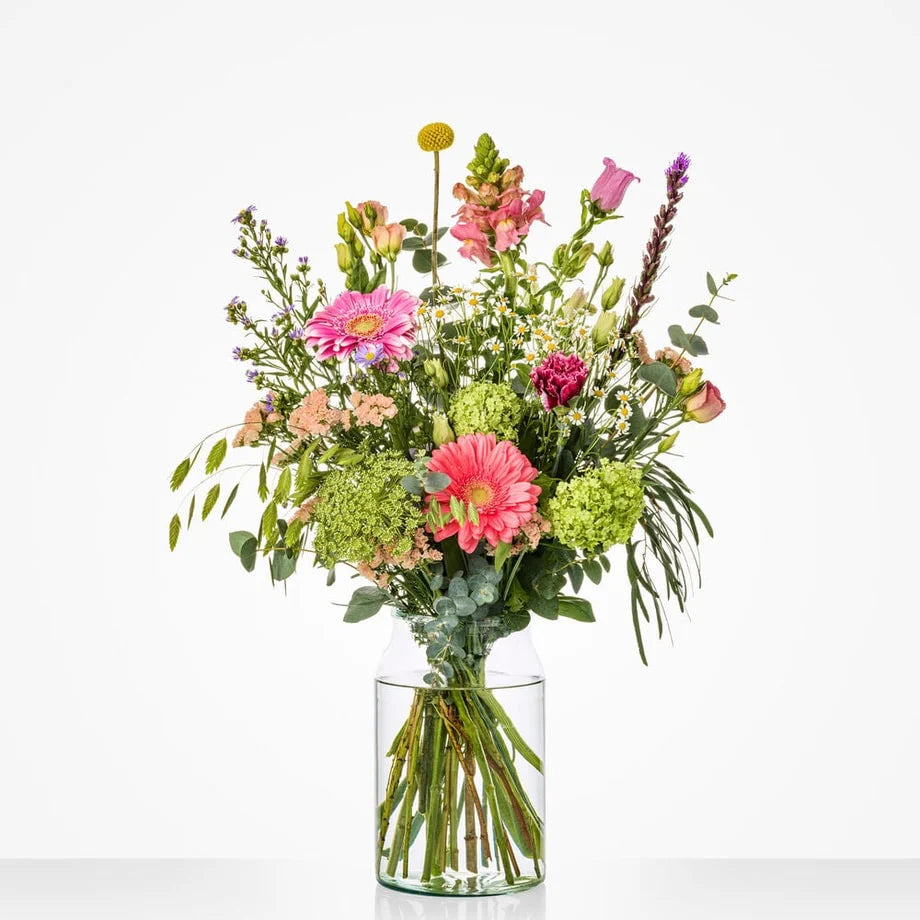 Gekleurd klein boeket in een glazen vaas met gerbera's, rozen en andere bloemen.