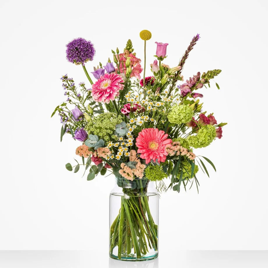 Gekleurd middelgroot boeket in een glazen vaas met gerbera's, rozen en andere bloemen.