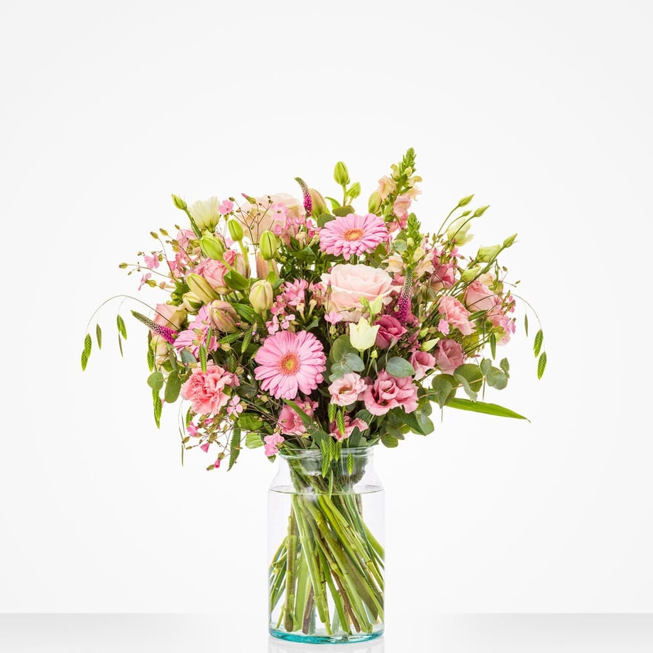 Groot boeket in een glazen vaas met roze gerbera's, rozen en andere bloemen.