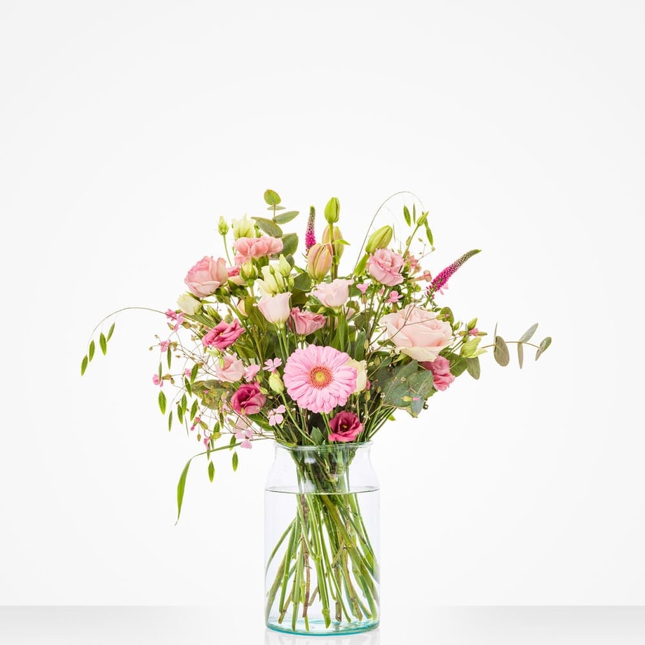 Klein boeket in een glazen vaas met roze gerbera's, rozen en andere bloemen.