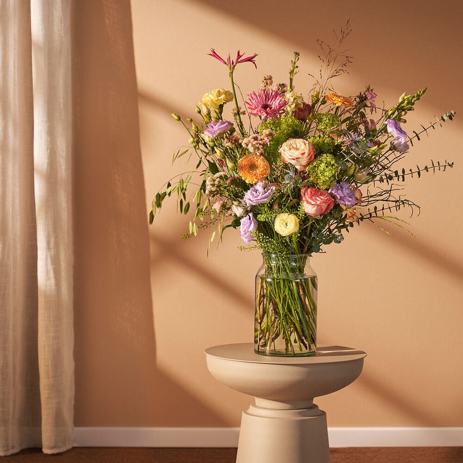 Voorjaarsboeket in glazen vaas op een stijlvolle tafel met warme lichtval