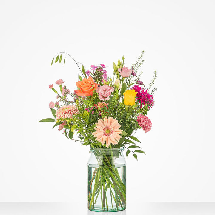 Klein boeket met diverse bloemen in pastel- en felle tinten, waaronder gerbera’s en rozen, gepresenteerd in een glazen vaas.