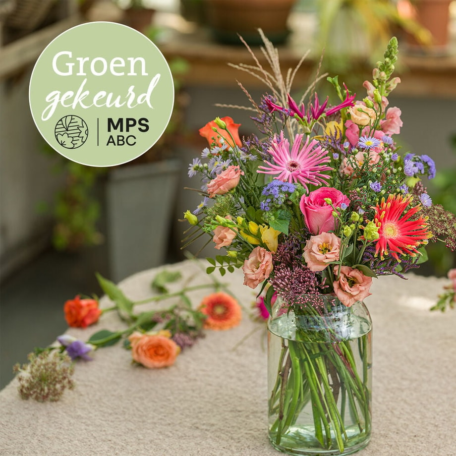 Boeket van felgekleurde bloemen zoals gerbera’s, rozen, en veldbloemen in een glazen vaas met een ‘Groen gekeurd’ MPS ABC-certificaat badge op de achtergrond.