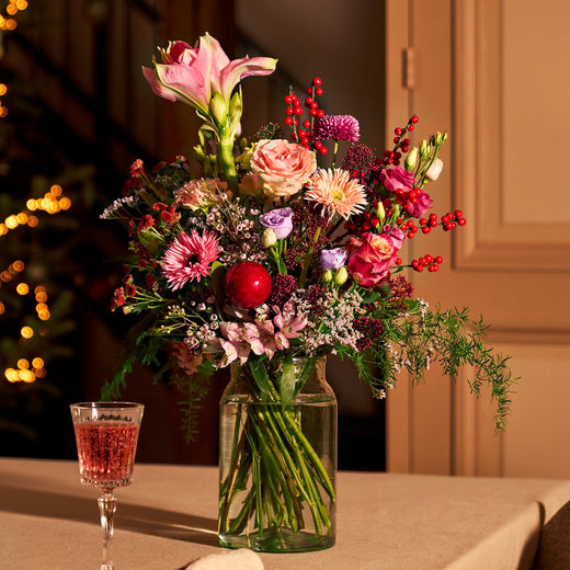 Feestelijk kerstboeket met rode bessen, rozen, amaryllis en seizoensbloemen in een glazen vaas.